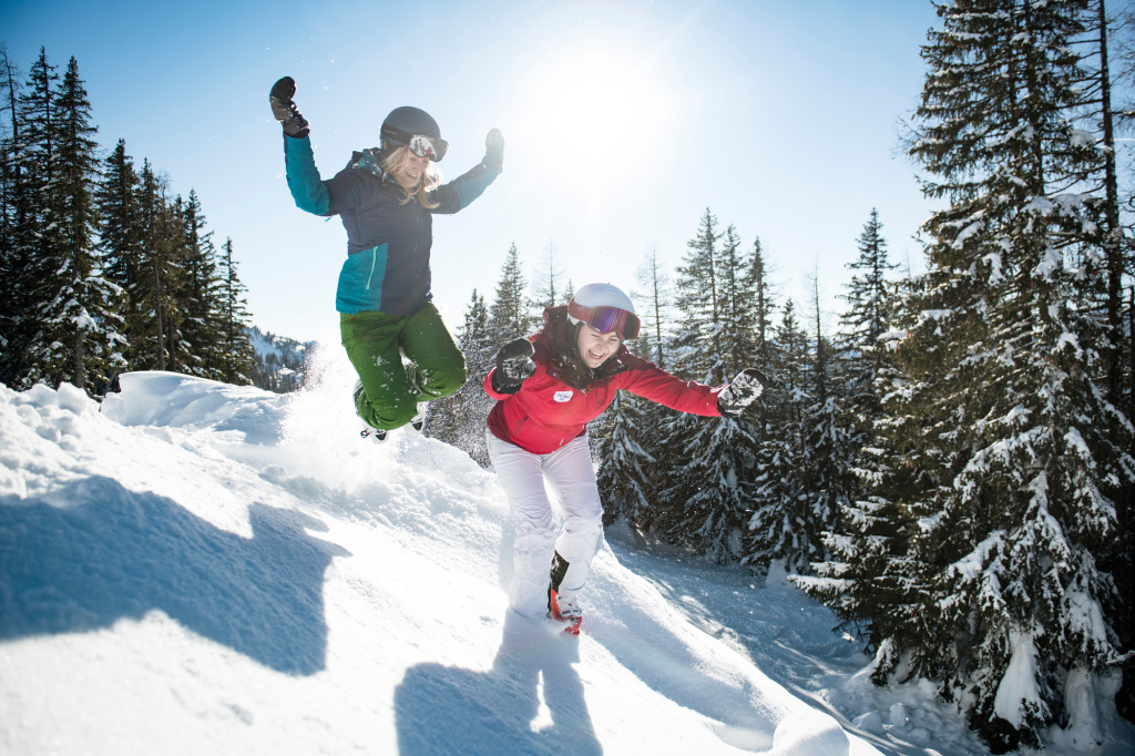 Zwei Personen springen lachend in frischem Pulverschnee