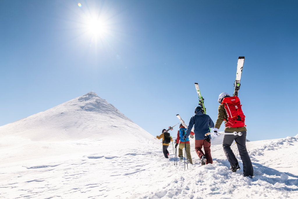 Gruppe von Skifahrern steigt bei Sonnenschein einen verschneiten Hang hinauf